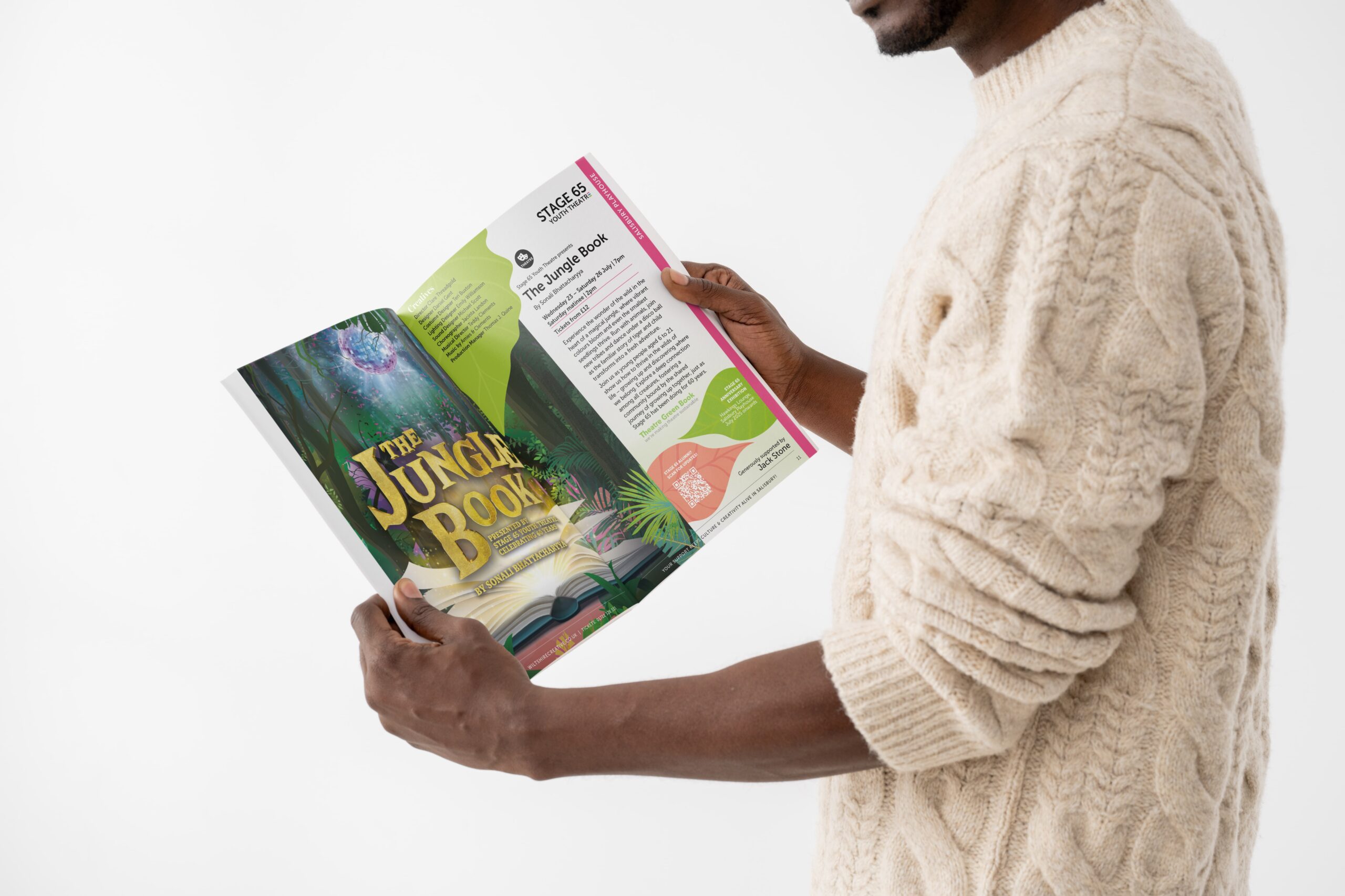 A man wearing a woolie patterned jumper holding Wiltshire creative's show brochure. The page is opened to show the Jungle book with a big image on one page and the marketing text on the other.
