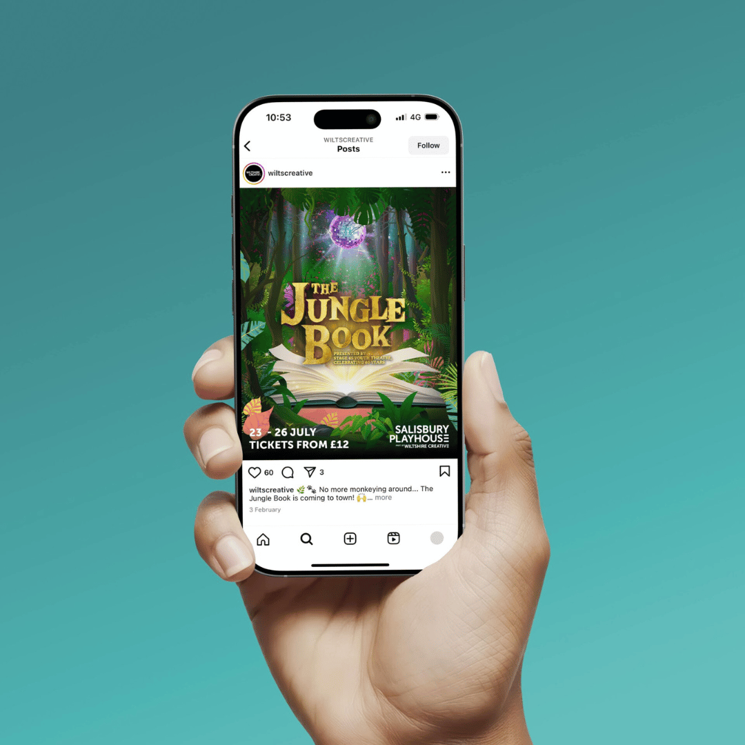 A hand holding a phone showing an Instagram feed. The feed shows a social post from Wiltshire creative promoting their jungle book show at the Salisbury Playhouse 23-26 July with tickets from £12. Image is mocked up on a turquoise background.