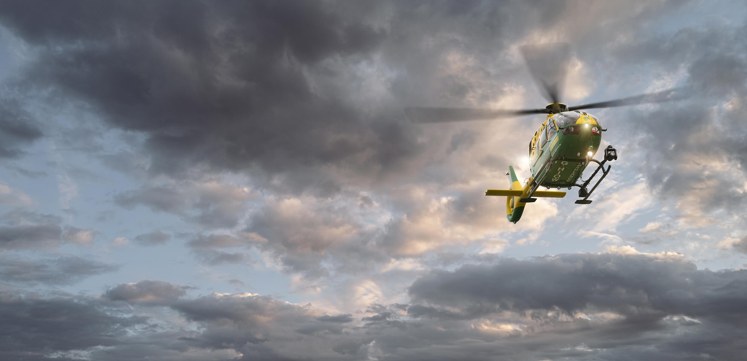 A photo of a HIOWAA helicopter flying through an overcast sky with breaks in the clouds showing blue skies