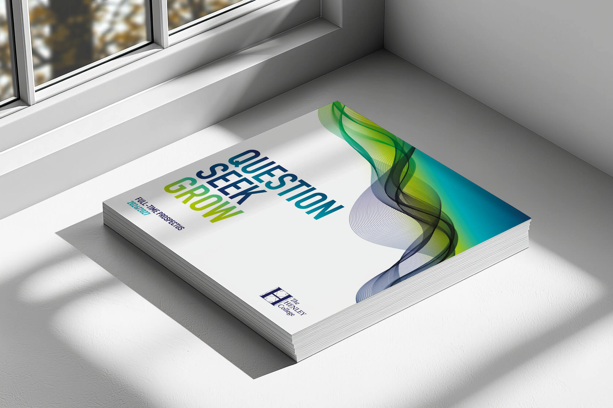 A mock-up of the Henley College Prospectus sat next to a window, with shadows and light shining on to it.