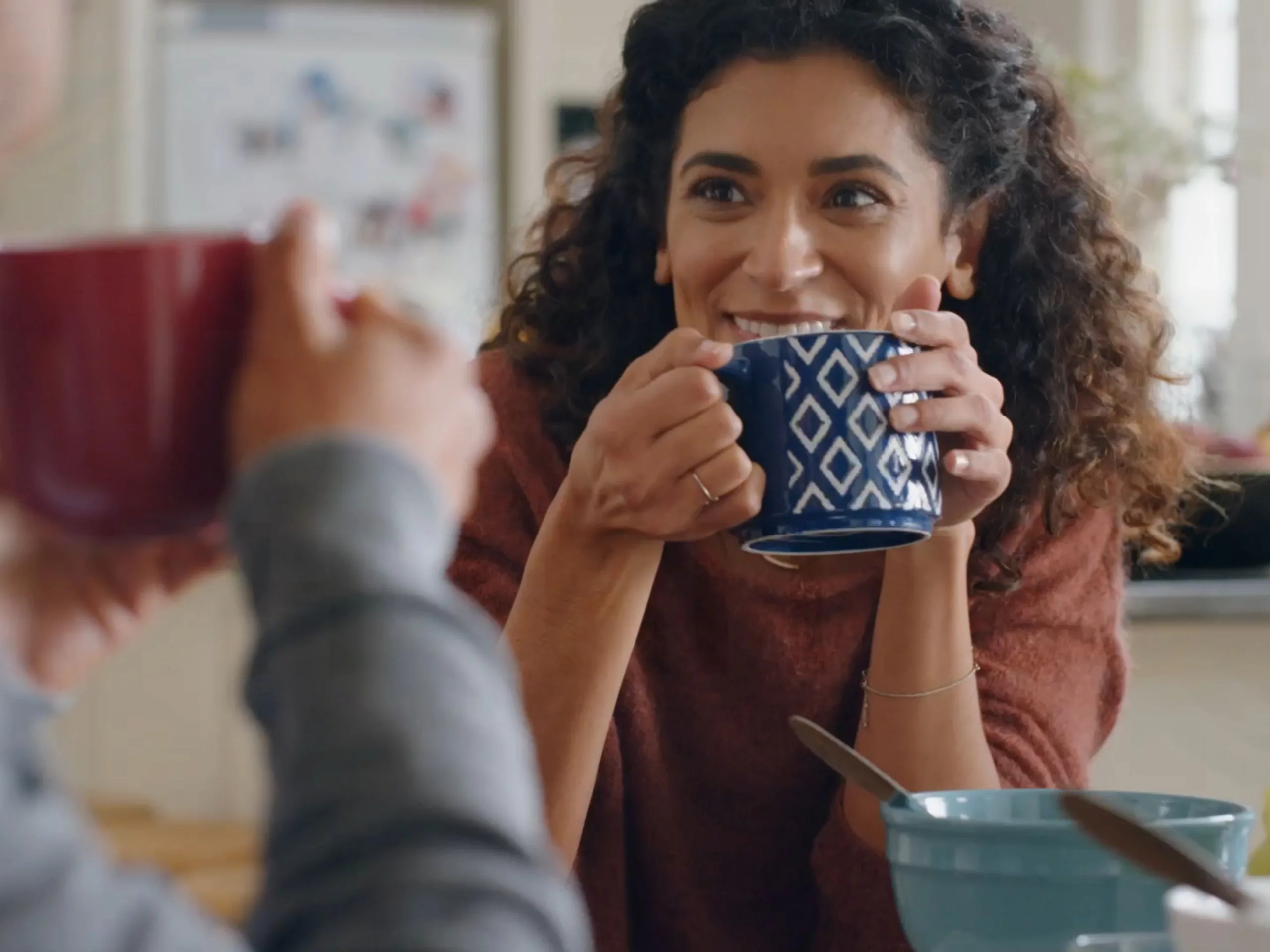 A woman talking to someone whilst drinking a hot drink.