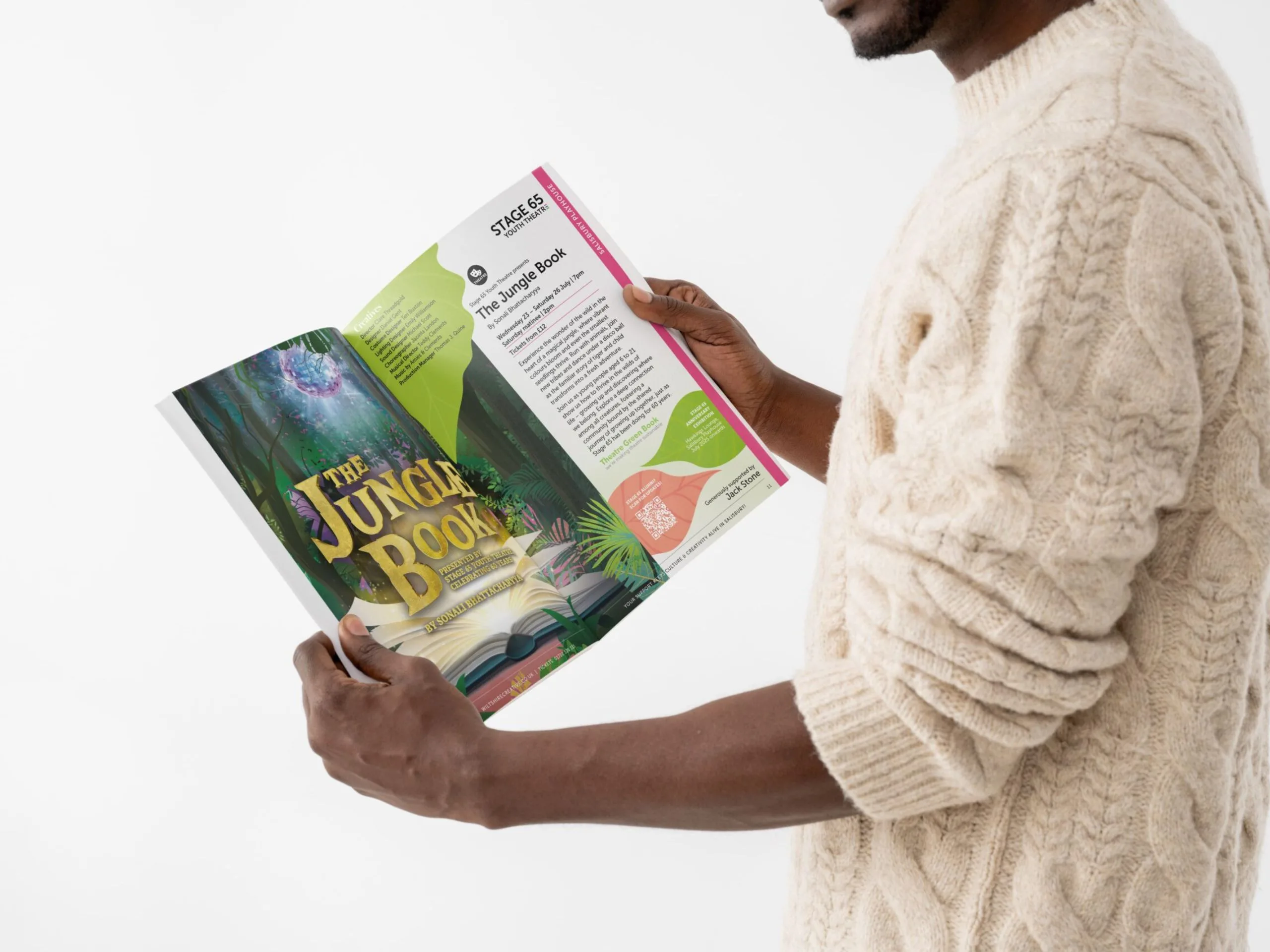 A man wearing a woolie patterned jumper holding Wiltshire creative's show brochure. The page is opened to show the Jungle book with a big image on one page and the marketing text on the other.